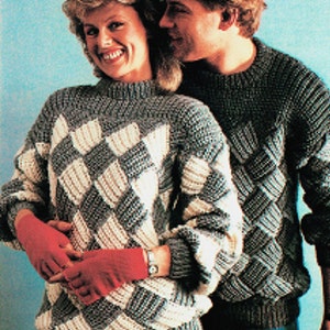 May include: Two people wearing matching gray and white knit sweaters with a diamond pattern. The sweaters have a ribbed collar and cuffs. The people are standing close together and smiling.