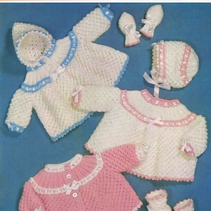 May include: A vintage baby knitting pattern showing a hooded jacket, sweater, hat, mittens, and booties. The garments are white and pink, with blue and pink trim. The pattern is for babies aged birth to 6 months.