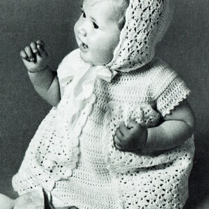 May include: A baby wearing a white, crocheted dress and bonnet. The dress has a round neckline and short sleeves. The bonnet is tied under the chin with a ribbon. The baby is sitting and looking to the side.