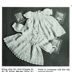 May include: A white knitted baby dress and matching cardigan with a delicate lace pattern. The dress has a gathered skirt and short sleeves. The cardigan has a button closure and a matching lace trim.