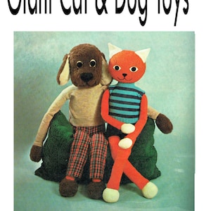 May include: A brown dog and an orange cat plush toy sitting on a green cushion. The dog is wearing plaid trousers and the cat is wearing a blue and white striped shirt. Giant Cat & Dog Toys.