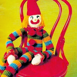 May include: A crocheted clown doll with a red hat, yellow hair, and a striped multi-coloured outfit sits on a red wooden chair.