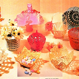 May include: A collection of crocheted baskets and bowls in various colors, including yellow, orange, pink, red, and white. The baskets are decorated with lace trim and some have handles. The bowls are filled with candy and flowers.