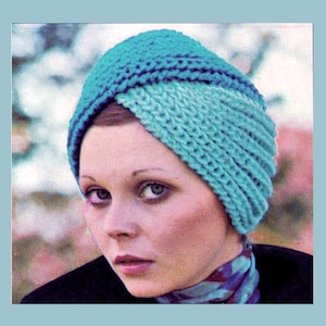 May include: A turquoise blue knitted turban style hat with a folded design. The hat is made of a soft, textured yarn.