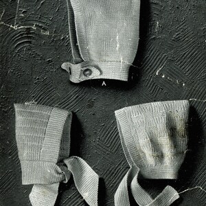 May include: Three knitted baby bonnets in white, with different styles of ties. The bonnets are made with Patons Super or Beehive Scotch Fingering, 4-ply yarn.