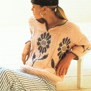 May include: A pink crocheted sweater with a floral design. The sweater has a V-neck and three-quarter sleeves. The model is wearing the sweater with a black hat and striped pants.