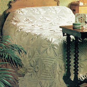 May include: A white crocheted bedspread with a floral pattern and fringe. The bedspread is on a bed with a wooden headboard.