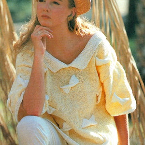 May include: A woman wearing a straw hat with a white trim and a yellow knitted sweater with a white collar and butterfly-shaped embellishments. She is wearing white trousers and sitting on a log.