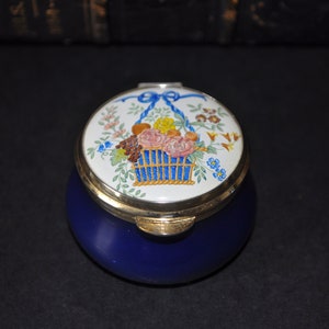 May include: A blue and white porcelain trinket box with a floral design on the lid. The lid features a basket of flowers with a blue ribbon.