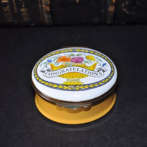 May include: A yellow and white oval trinket box with a floral design and the word "CONGRATULATIONS" on the lid.