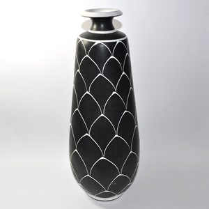 May include: A black ceramic vase with a white geometric pattern. The vase has a rounded bottom and a narrow opening.