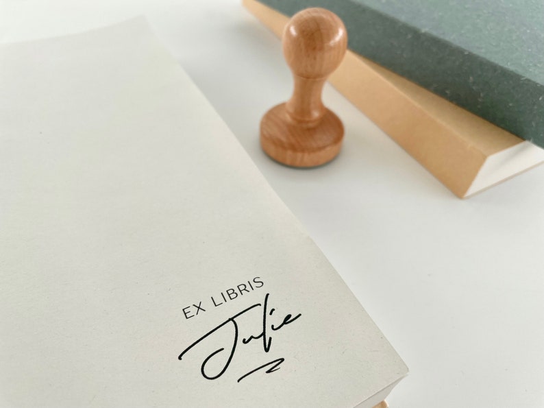 May include: A wooden book stamp with the text "Ex Libris" and a handwritten signature that says "Julie".