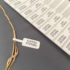 Może przedstawiać: Złoty naszyjnik o delikatnym wzorze z małymi diamentami. Naszyjnik jest prezentowany na szarym tle z białymi prostokątnymi naklejkami z napisem "Custom Stickers".