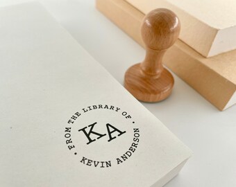 May include: A wooden stamp with a circular design that reads "From the Library of.  KA Kevin Anderson".