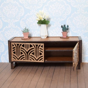 Könnte beinhalten: Miniatur-Holzschrank mit Art-Deco-Design an der Tür. Der Schrank ist braun mit einer hellbraunen Dekorplatte. Er hat ein Regal im Inneren und ist mit kleinen Topfpflanzen und einer weißen Vase mit Blumen dekoriert.