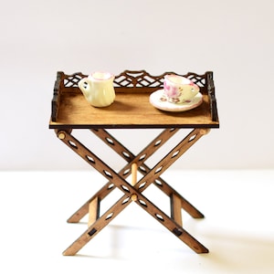 May include: A wooden folding table with a decorative top and a white teacup and saucer on the surface.