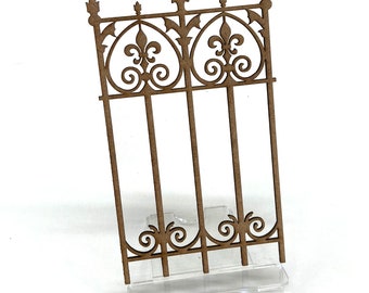 May include: A wooden cutout of a decorative fence with a fleur-de-lis design. The fence is made of thin wood and has a brown color.