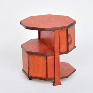 May include: A miniature wooden side table with an octagonal top and base, featuring a reddish-brown finish. The structure includes a central vertical support connecting the top and bottom tiers, with a small drawer integrated into the upper section.
