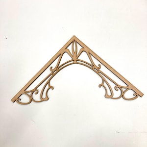May include: A wooden decorative corner piece with a cutout design. The piece is shaped like a triangle with a curved top and intricate details.