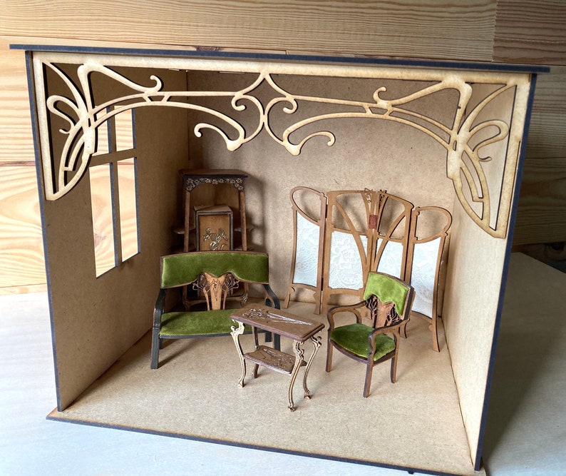 May include: A miniature dollhouse room with a green velvet sofa, a green velvet armchair, a wooden table, and a decorative screen. The room is made of wood and has a decorative wooden archway.