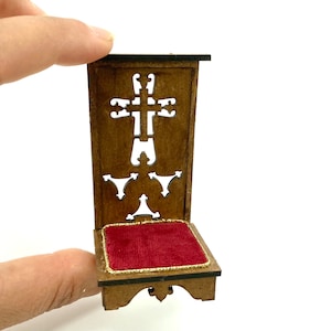 Può includere: Un piccolo inginocchiatoio in legno con un cuscino in velluto rosso e un'incisione a forma di croce sul retro.
