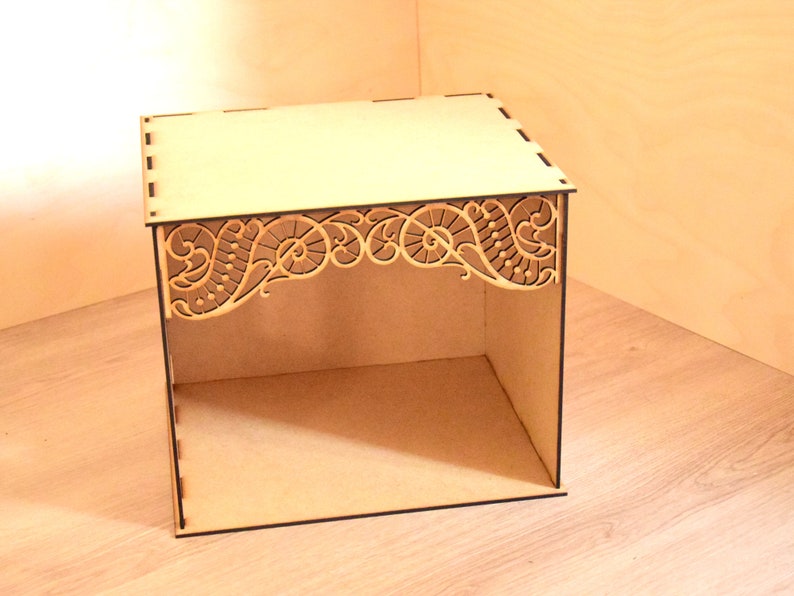 May include: A small wooden box with a decorative, intricate, laser-cut design on the top edge. The box is open and has a shelf inside.