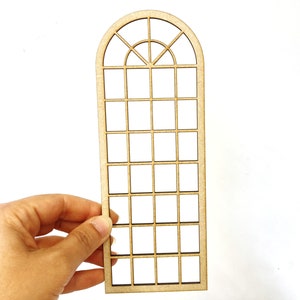 Puede incluir: Un marco de ventana arqueado de madera con un patrón de rejilla. El marco está hecho de madera de color marrón claro y tiene una serie de pequeñas aberturas cuadradas. La parte superior del marco tiene un diseño curvo y arqueado con detalles adicionales.