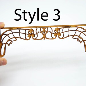 May include: A wooden decorative arch with a delicate, intricate design. The arch is made of thin, laser-cut wood and features a repeating pattern of swirls and curves. The arch is a light brown color and has a slightly distressed finish. Style 3.