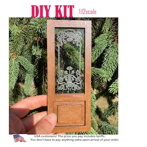 Könnte beinhalten: Ein 1:12-Bausatz bestehend aus einer rechteckigen braunen Holztürplatte mit einem klaren Glaseinsatz. Das Glas zeigt ein filigranes, weiß graviertes Blumen- und Rankenmuster. Der Text DIY KIT 1:12scale ist oben aufgedruckt.