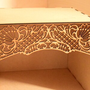May include: A wooden box with a decorative, laser-cut design on the top. The design features intricate floral patterns and a latticework.