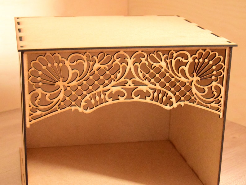 May include: A wooden box with a decorative, laser-cut design on the top. The design features intricate floral patterns and a latticework.