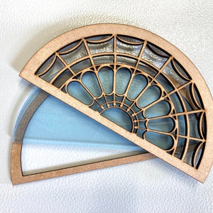 May include: A wooden, half-circle box with a decorative, geometric, stained glass design. The box is open and the lid is lying on top of the box.