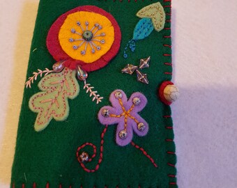 May include: A green felt pouch with a red stitched border. The pouch is decorated with colorful felt flowers, leaves, and beads.