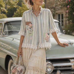 May include: A light blue and white striped button-down shirt with a ruffled collar, lace-trimmed sleeves, and hem, featuring floral and bird fabric patches. A cream-coloured tiered skirt with lace inserts and a matching lace handbag with fabric flowers.
