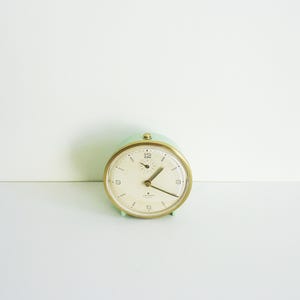 May include: A vintage green alarm clock with a white face and gold hands. The clock has a round shape and a simple design.
