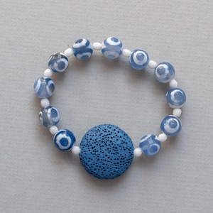 May include: A blue and white agate bead bracelet with a blue lava rock charm. The bracelet is made with white spacer beads and has a blue and white agate bead pattern.