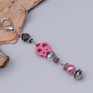 May include: A pink skull charm with silver and black beads on a silver chain with a lobster clasp.
