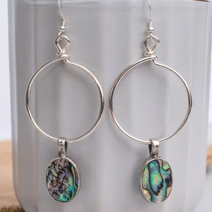 May include: Silver hoop earrings with a dangling oval abalone shell pendant. The shell has iridescent green, blue, and purple colors.
