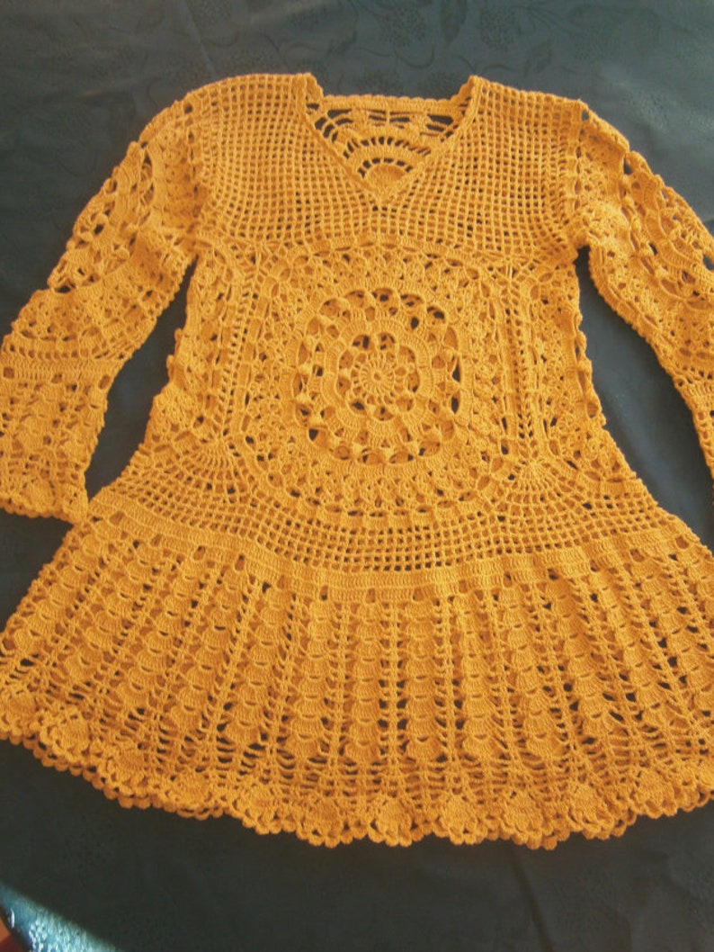 May include: A mustard yellow crocheted top with long sleeves and a round, lacy design in the center.