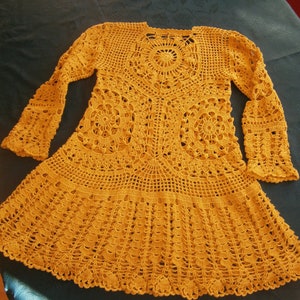 May include: A mustard yellow crocheted dress with a round, lacy design in the center and long sleeves.