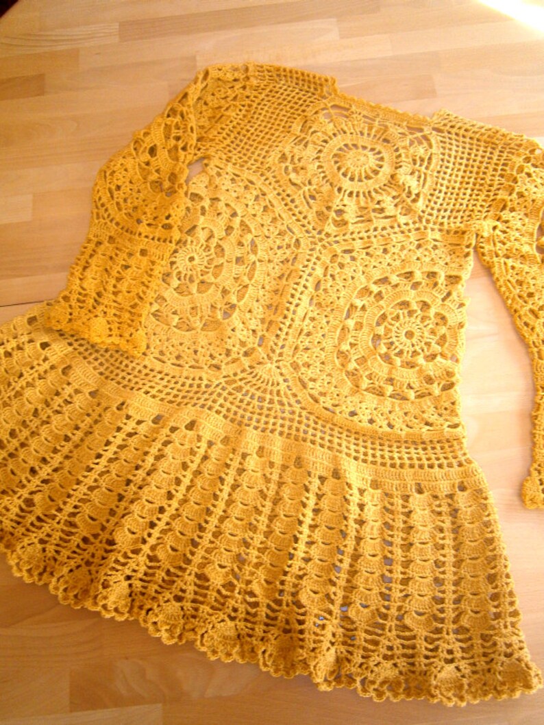 May include: A yellow crocheted top with long sleeves and a flared skirt. The top is made with a delicate, lacy pattern.