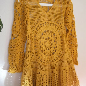 May include: A yellow crocheted top with a V-neck and long sleeves. The top has a circular pattern in the center and a scalloped hem.
