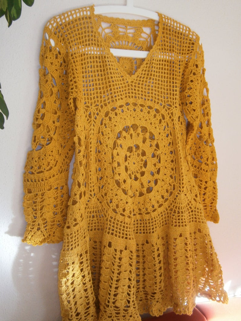 May include: A yellow crocheted top with a V-neck and long sleeves. The top has a circular pattern in the center and a scalloped hem.
