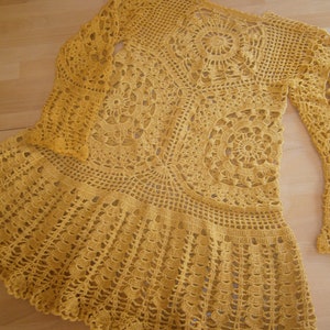 May include: A yellow crocheted dress with a long-sleeved top and a flared skirt. The dress is made with a delicate, openwork pattern.