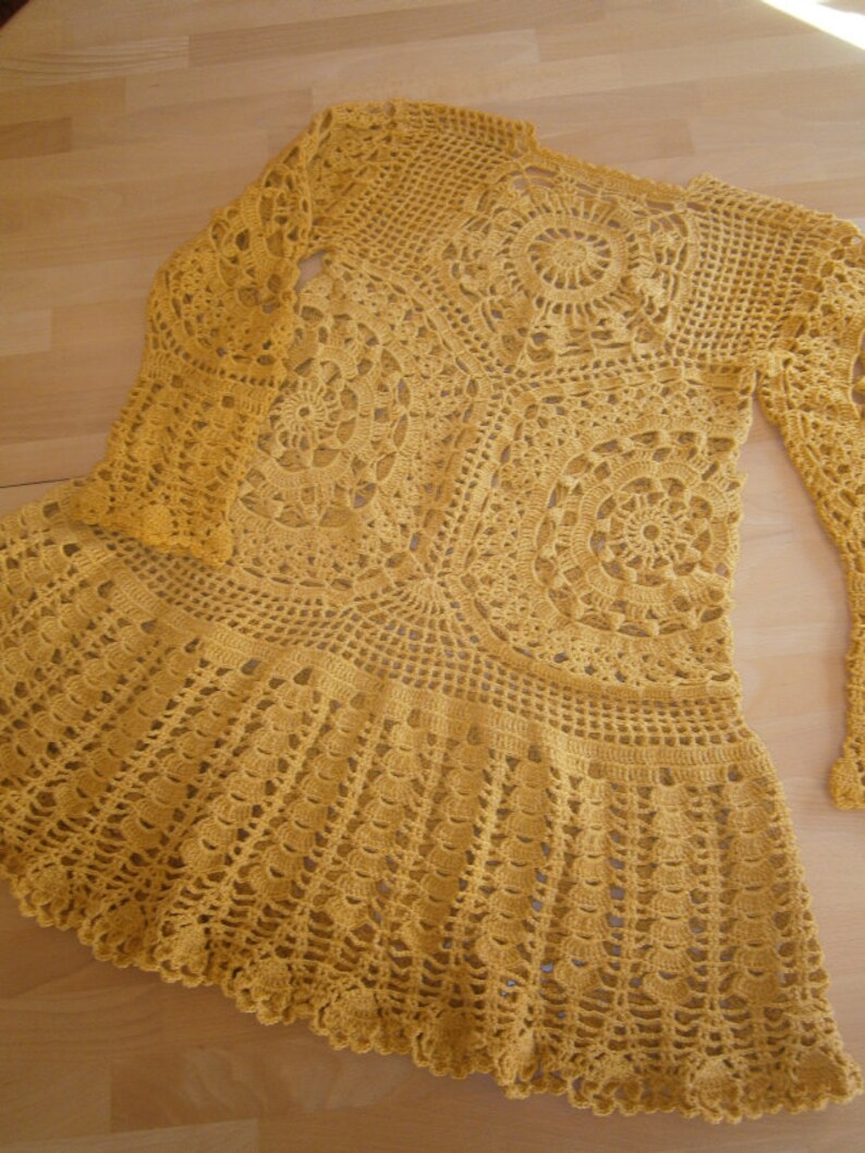 May include: A yellow crocheted dress with a long-sleeved top and a flared skirt. The dress is made with a delicate, openwork pattern.