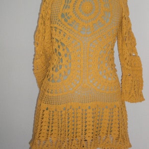 May include: A mustard yellow crocheted cardigan with a lacy design and long sleeves. The cardigan has a round neckline and a scalloped hem.