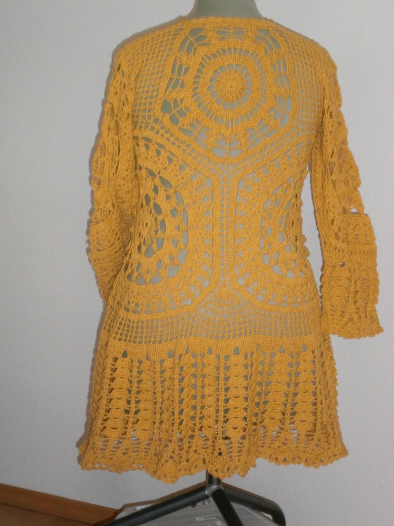 May include: A mustard yellow crocheted cardigan with a lacy design and long sleeves. The cardigan has a round neckline and a scalloped hem.