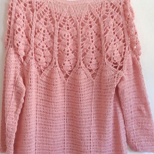 May include: A pink crocheted sweater with a lacy design around the neckline and sleeves.