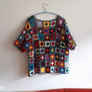 Peut inclure: Un haut en crochet gris avec un motif carré dans différentes couleurs, notamment le rouge, le bleu, le vert, le jaune et l'orange. Le haut a des manches courtes et un col carré.