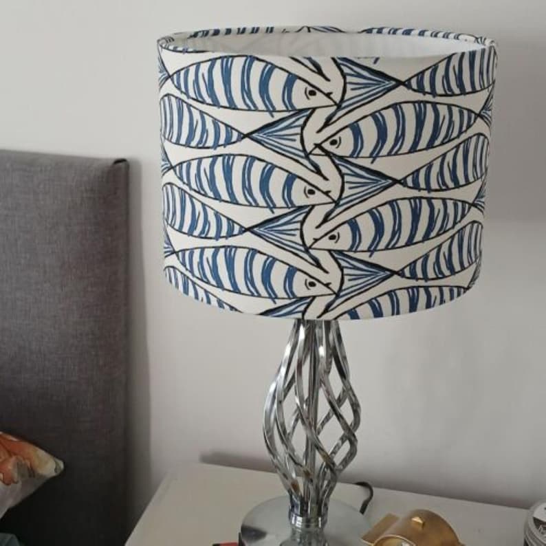 May include: A white lampshade with a blue and white fish pattern. The lampshade is on a silver, twisted metal base.